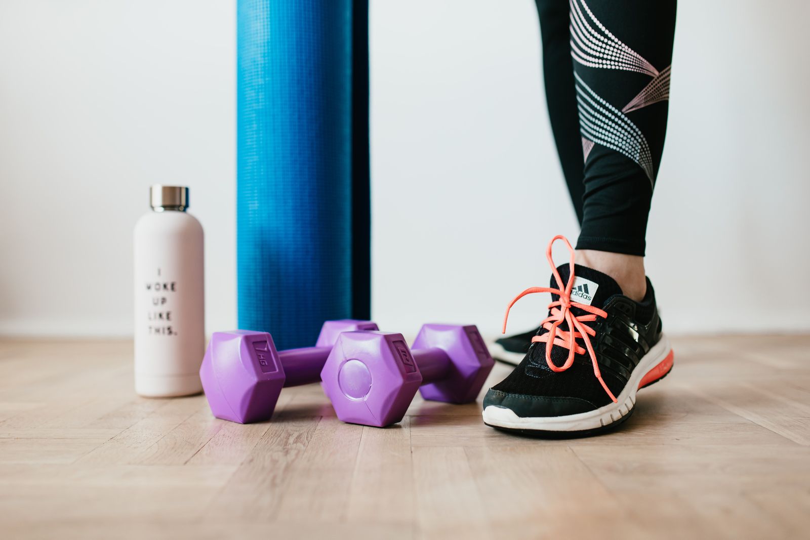 Purple hex dumbbells, a rolled blue exercise mat and a water bottle beside a trainer-clad foot